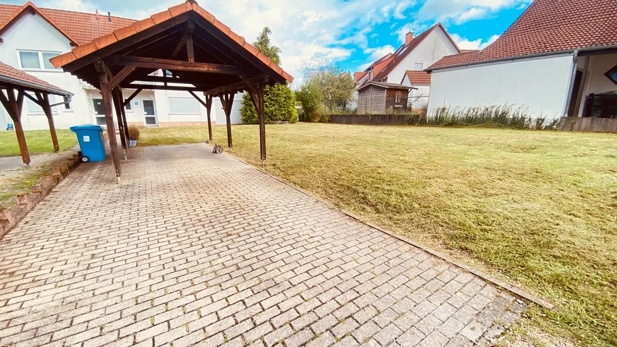 Gepflasterte Zufahrt mit Carport und angrenzender Rasenfläche